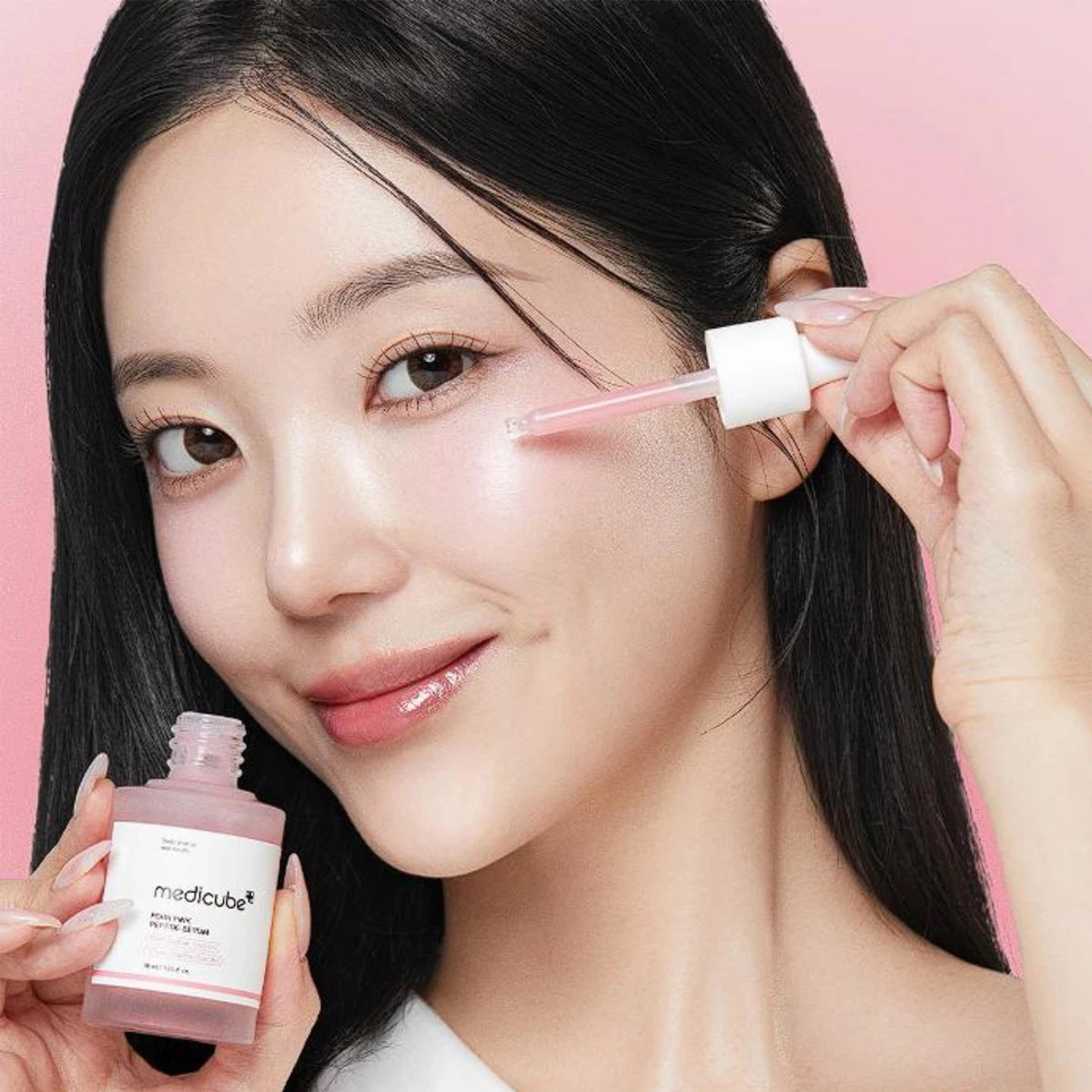Woman applying skincare product with a dropper and bottle against a pink background
